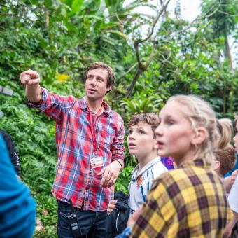 A group of school pupils standing looking in the direction of the teacher who is pointing